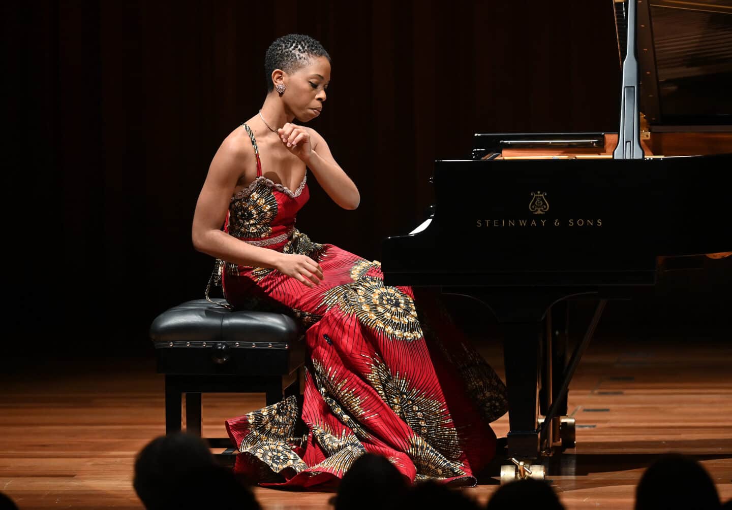 Image of Samantha Ege, a woman in a patterned red dress sitting at a piano, her hands raised in a dramatic motion