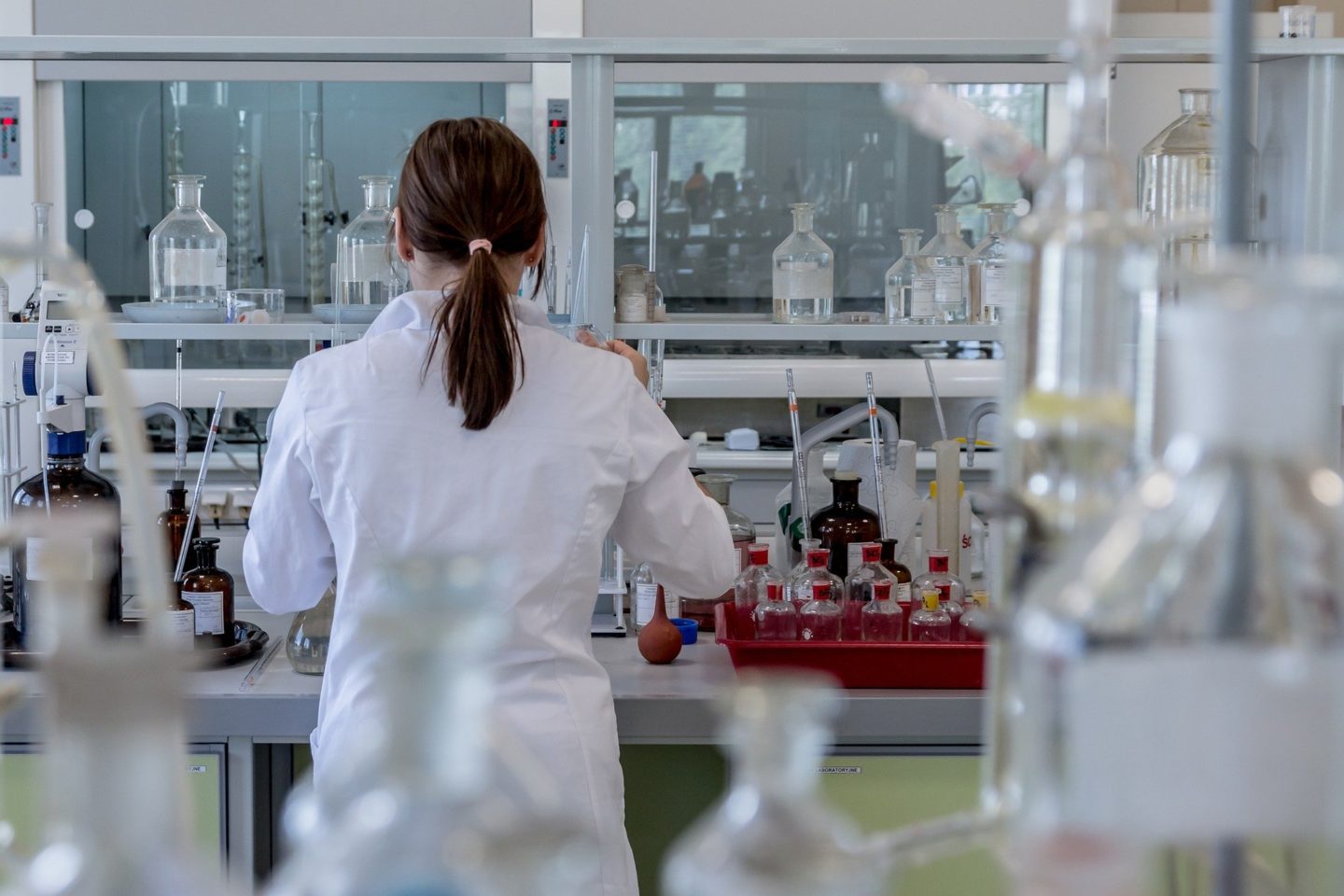 Image from behind of a woman in a white lab coat working in a lab