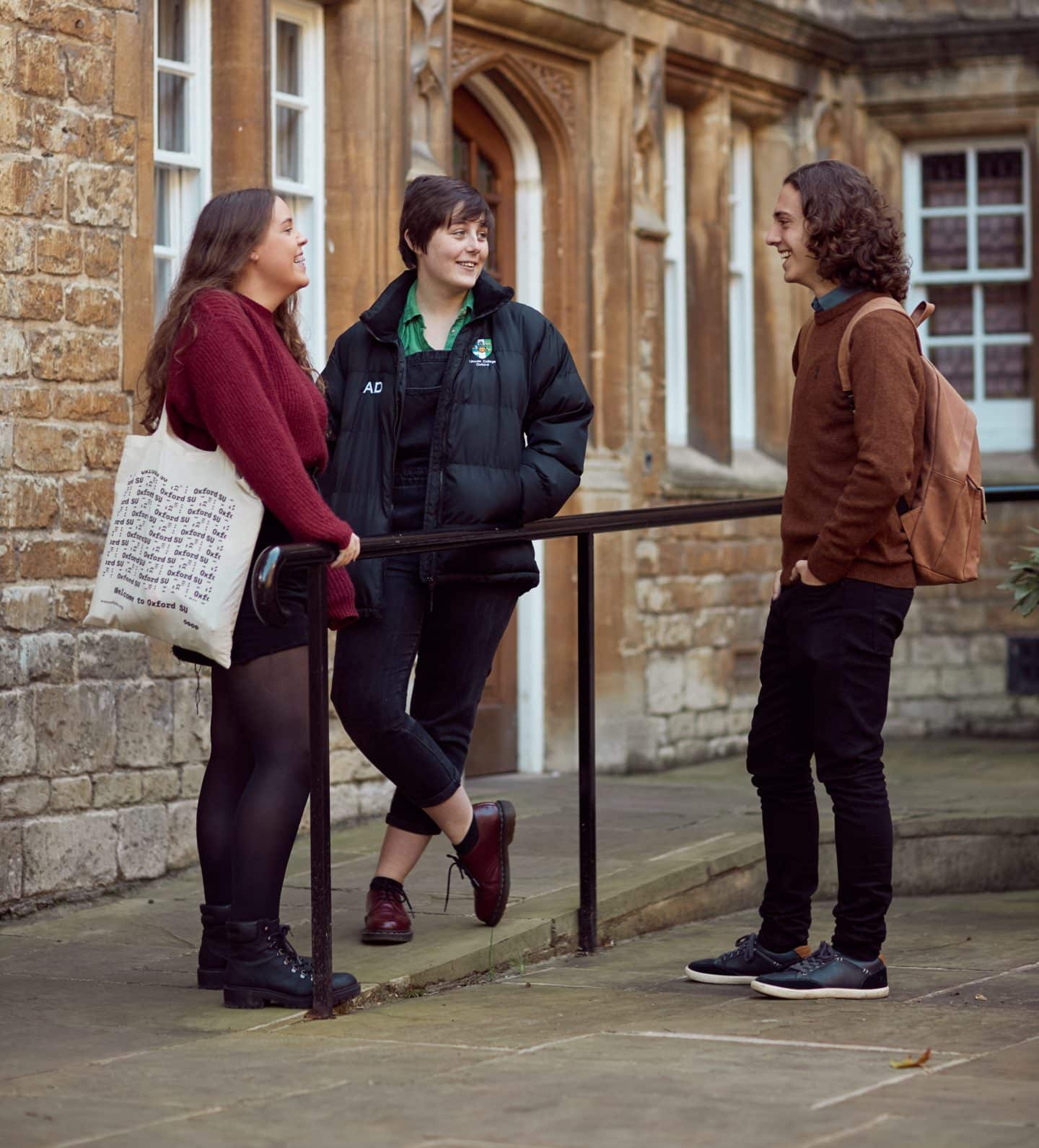 Three young students standing and chatting by a railing