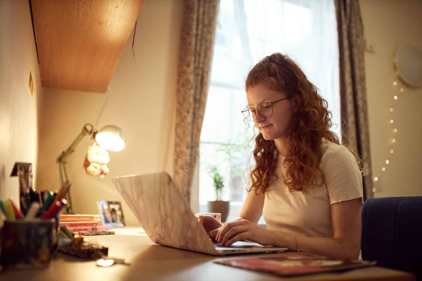 A student sitting at an open laptop in a bedroom