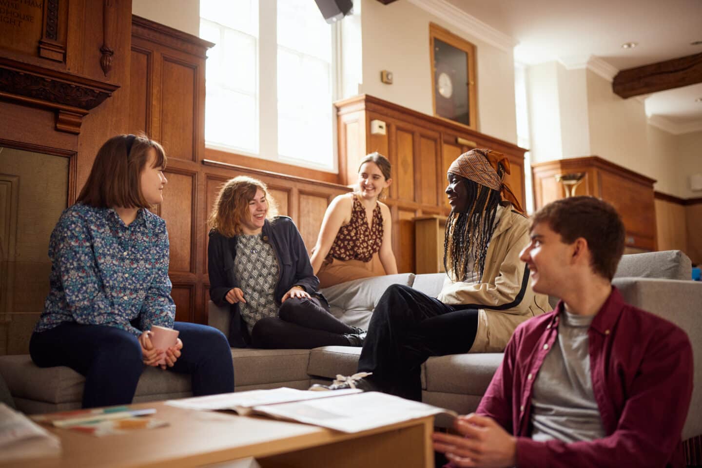 A group of five smiling students sitting around a sofa in the bright, wood-panelled Lincoln College Junior Common Room