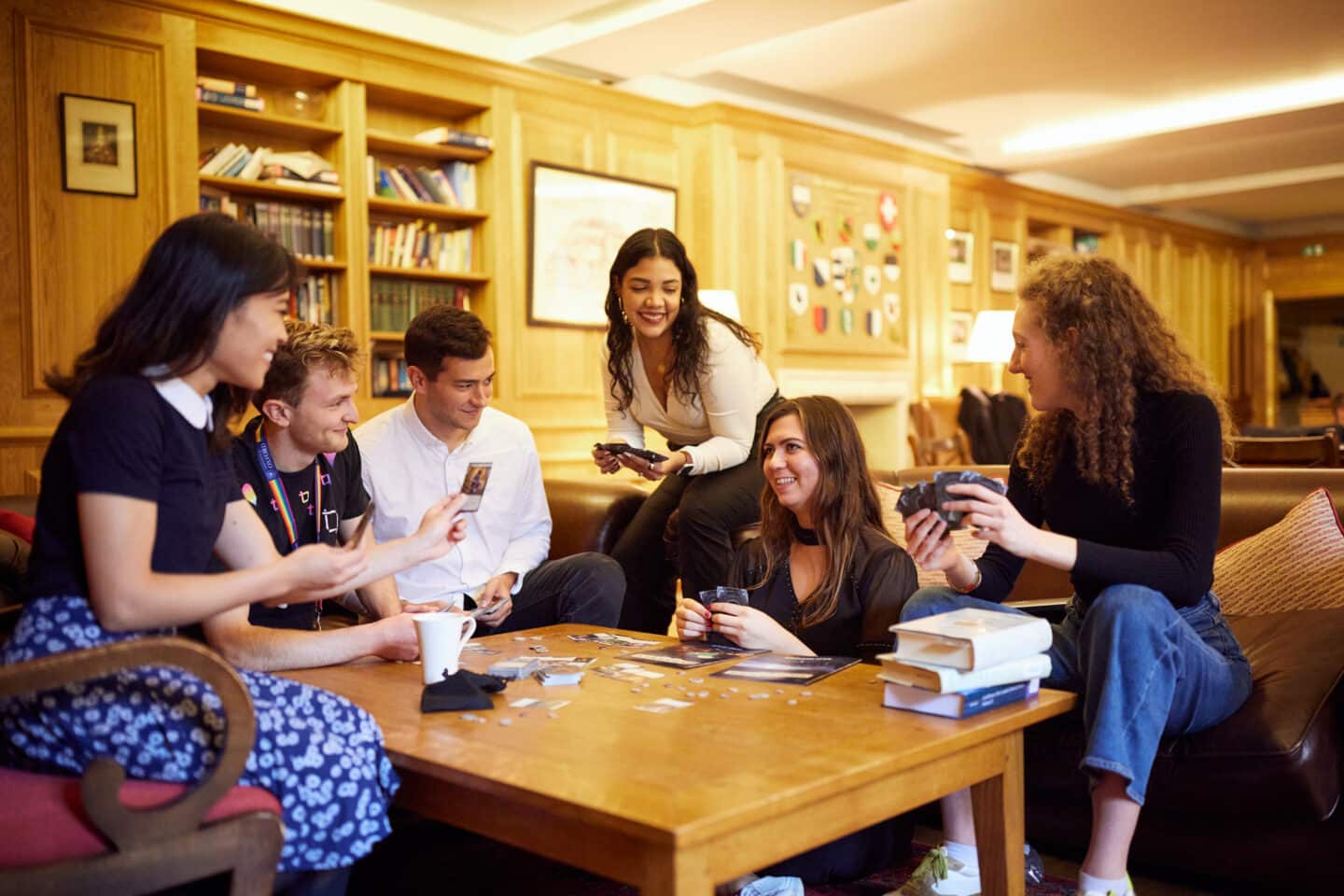 Six smiling students in the beautiful wood-panelled Lincoln College Middle Common Room, playing cards around a table