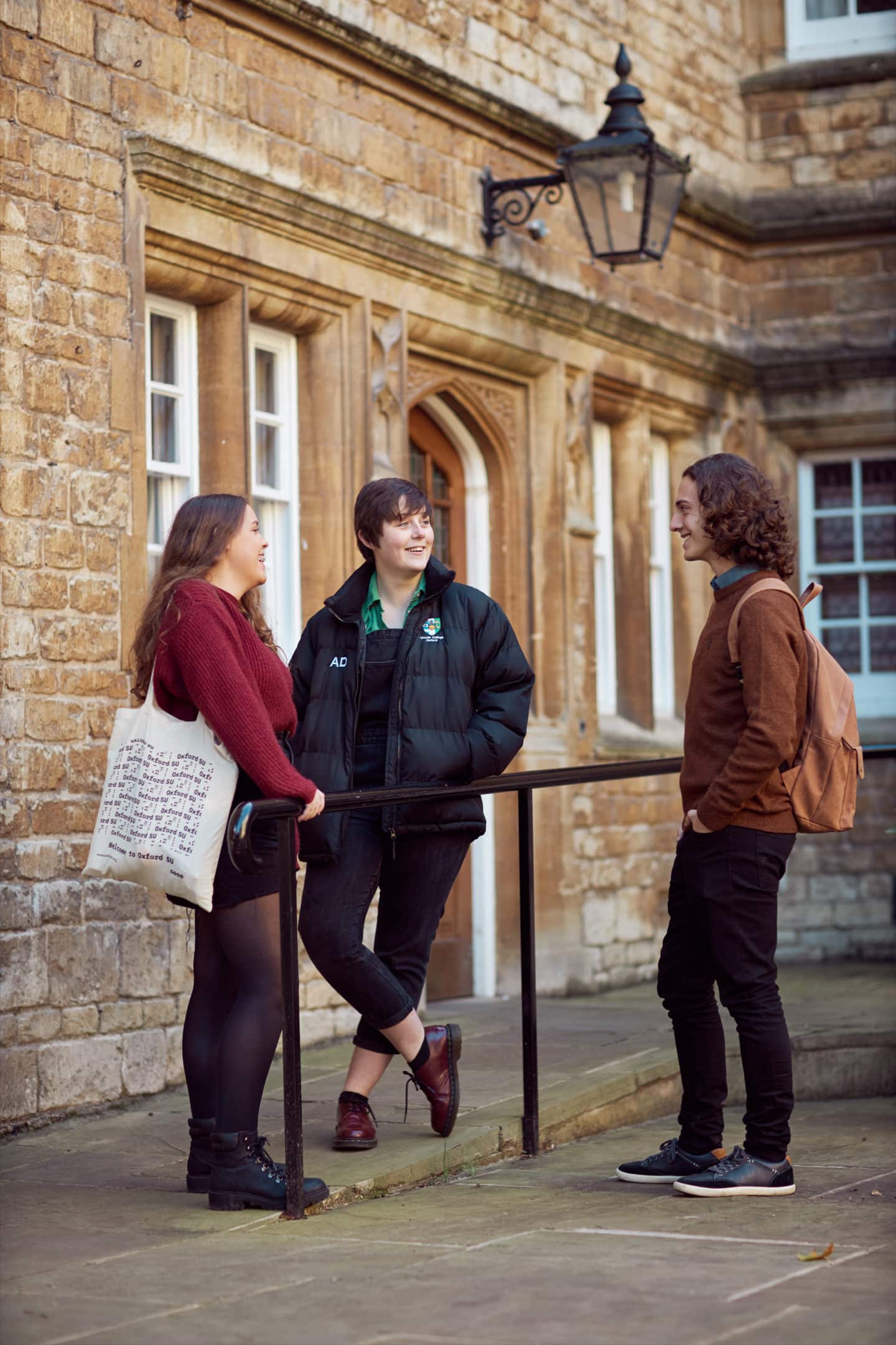 Three students talking by a rail in Lincoln College