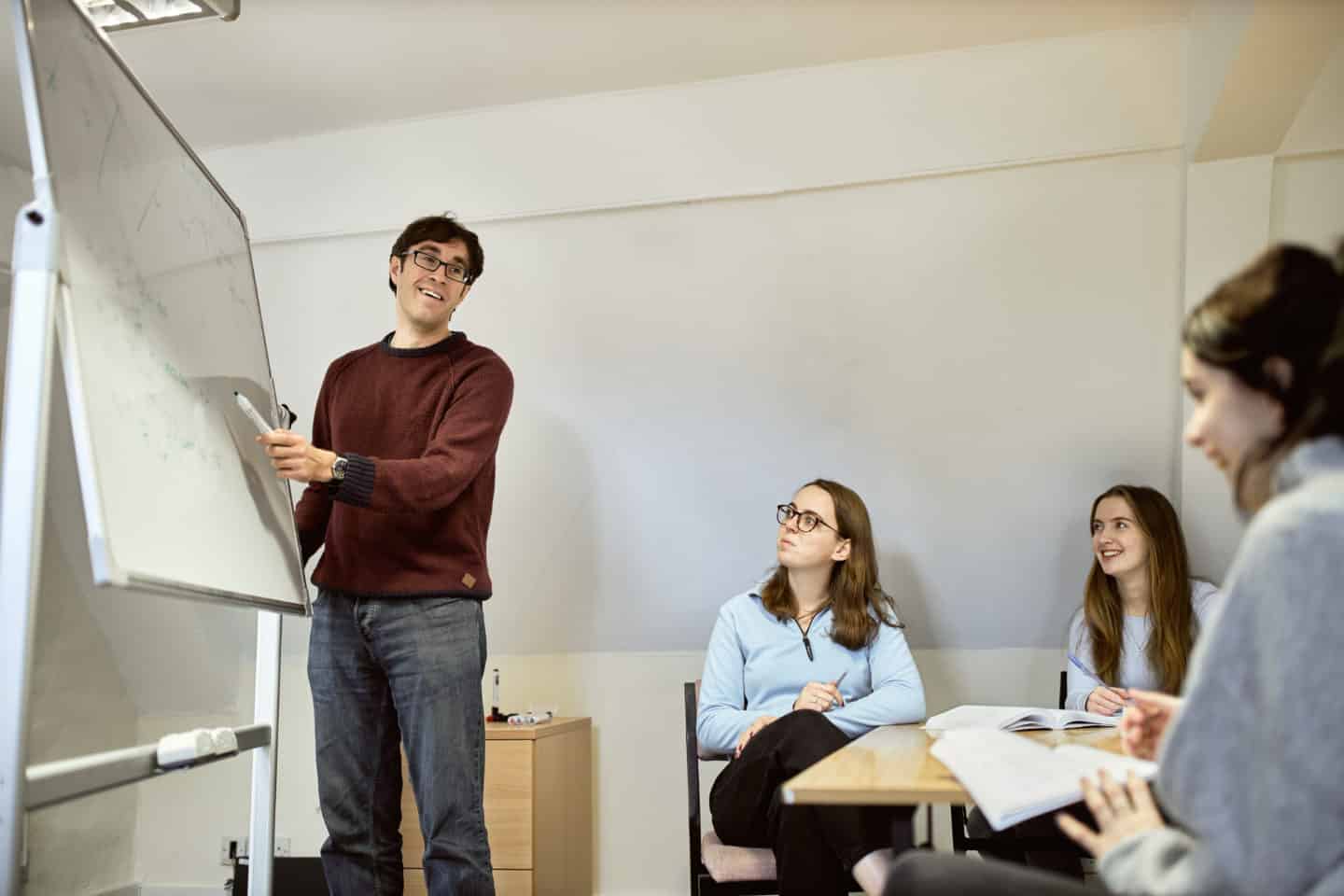 Students and their tutor working on a maths problem on a whiteboard