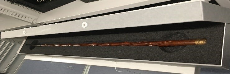 A long ornate wooden walking stick in a box