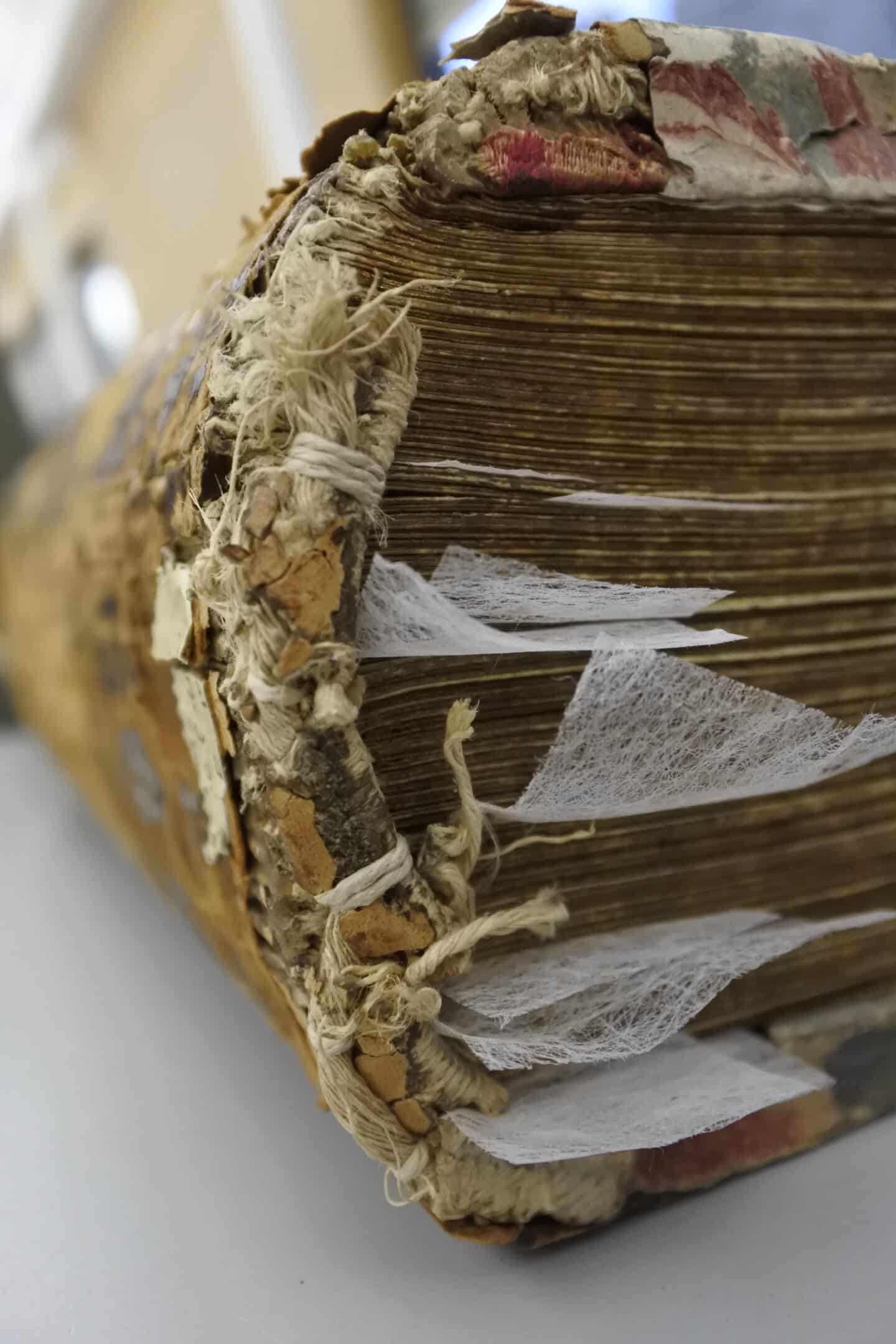 An old book of Greek Gospels in the middle of a restoration process, depicted closed with several sheets of thin Japanese paper between the pages.